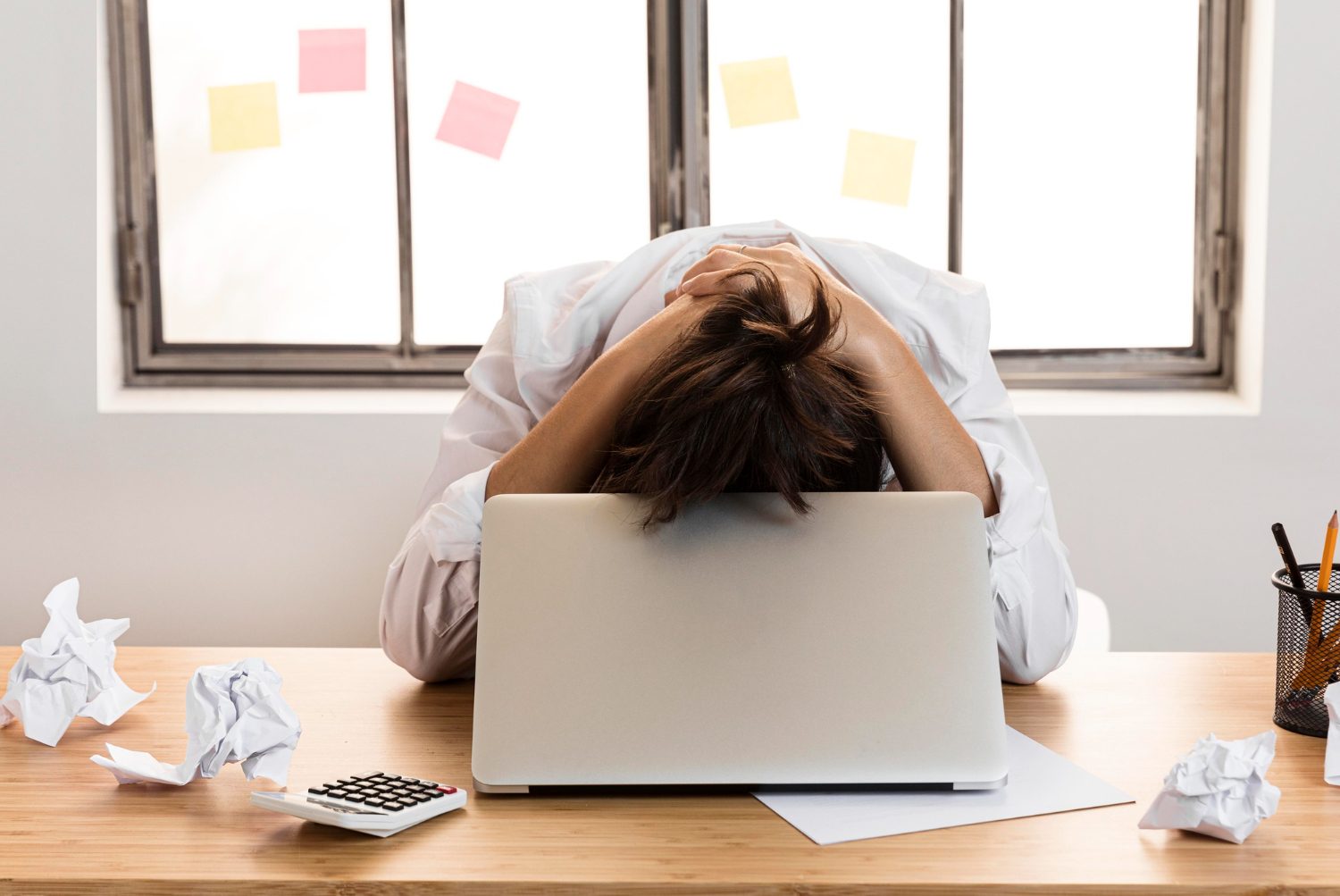 Frustrated person with head in hands at a desk with laptop and papers, symbolising stress and overwhelm at work