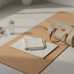 Yoga mat setup with beige towel, water bottle, and canvas bag on light wooden floor