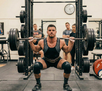 Man performing a heavy barbell squat in a gym, surrounded by onlookers, demonstrating strength and focus