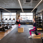 Women exercising in a modern gym, performing squats and lunges, surrounded by equipment and weights