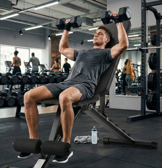 Man lifting dumbbells on an incline bench at the gym with workout equipment and people in the background